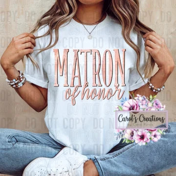 Person wearing a white t-shirt with 'Matron of Honor' text, sitting on a wooden floor.