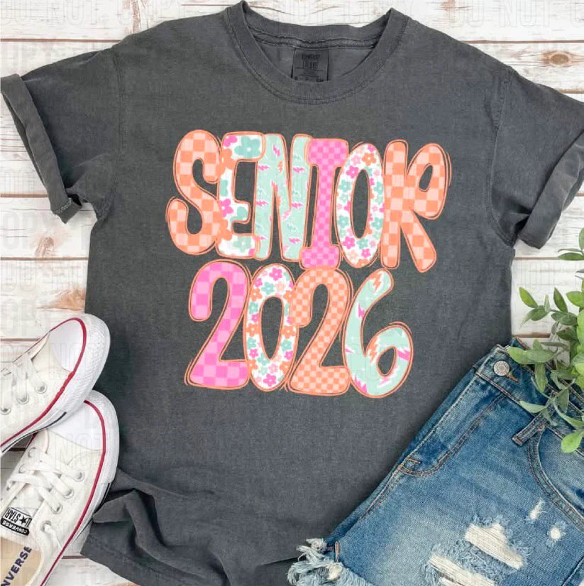 Gray t-shirt with 'Senior 2026' text on a wooden surface with sneakers and jeans.
