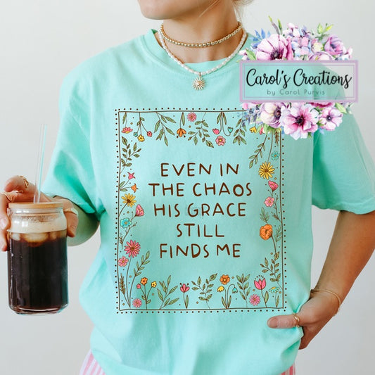 Person wearing a teal t-shirt with floral design and text, holding a drink.